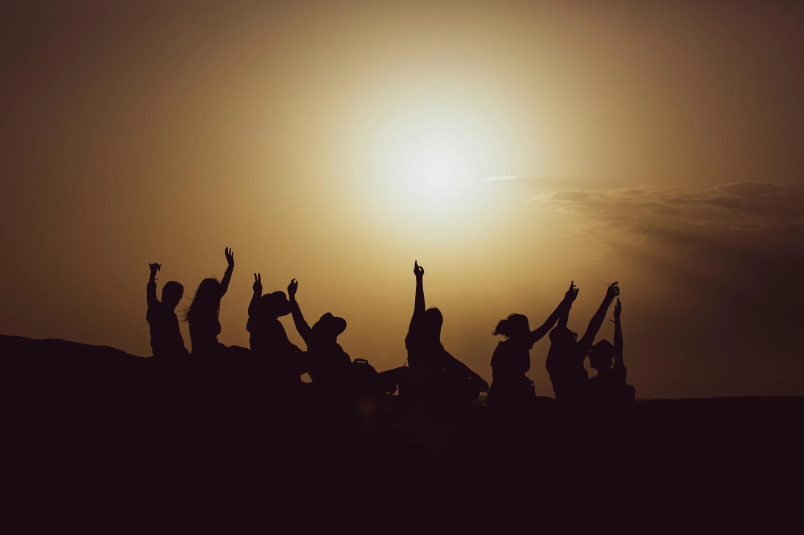 Des amis les bras levés sur une dune, au coucher du soleil